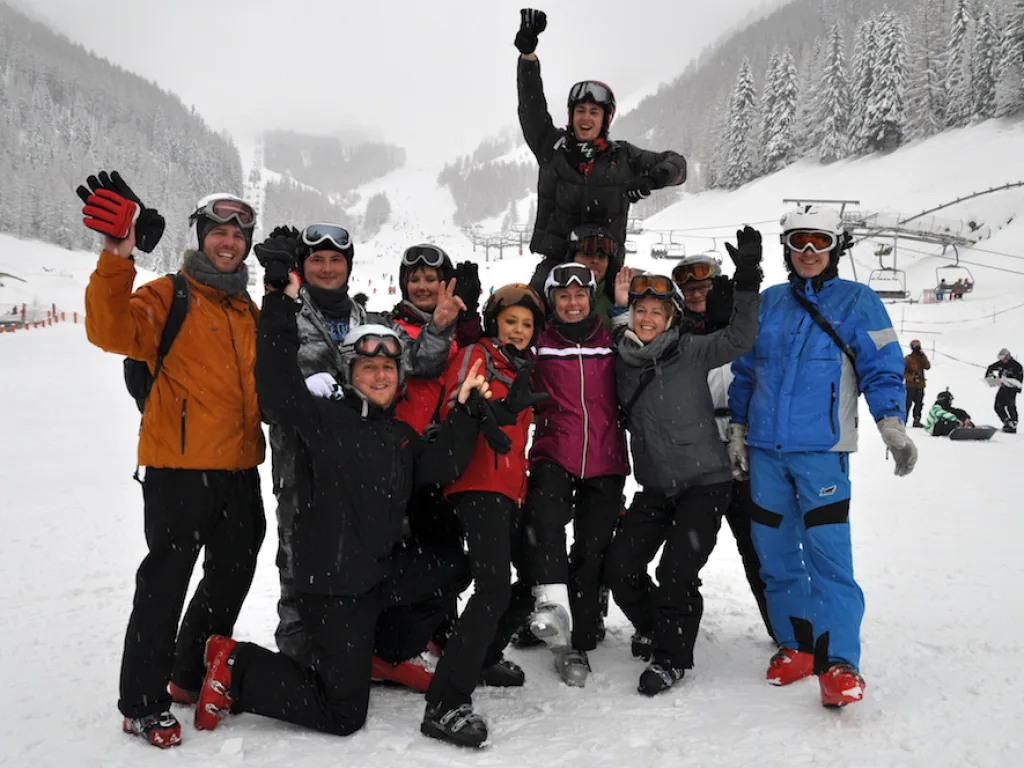Gruppe posiert jubelnd im Schnee vor der Piste.